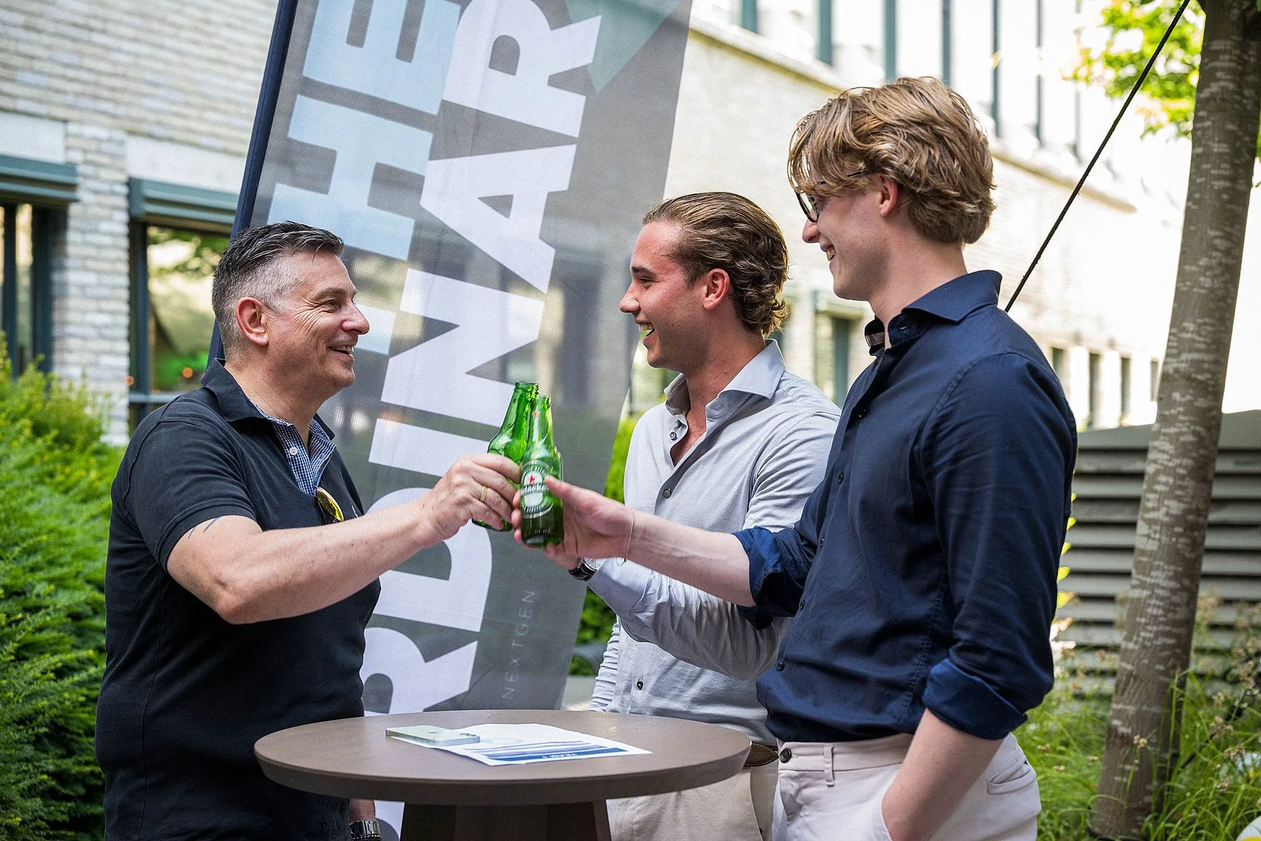Drie mannen proosten met een flesje bier op een buitenborrel